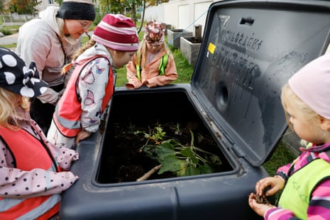 A woman and several children wearing hi-vis look into a compost bin