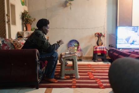 Side view of Nadir sitting on a sofa in a living room watching TV.