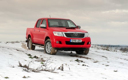 A bright red pickup truck driving offroad on a snowy hillside
