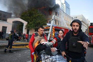Emergency workers carry away a casualty as smoke rises in the background