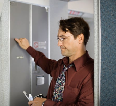 A man holding a toothbrush knocking on an aircraft toilet door