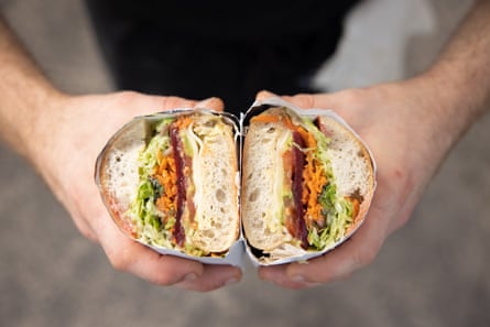 Close-up of hands holding a slice salad sandwich wrapped in white paper
