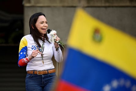 María Corina Machado speaks into a microphone with a Venezuelan flag in the foreground