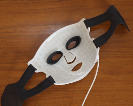 A CurrentBody Series 3 LED face mask with black straps lies on a wooden surface