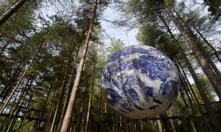 A huge globe, like a photo-realistic model of the Earth, suspended in a clearing, surrounded by tall trees