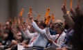 people hold up orange pieces of paper during a vote