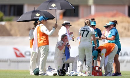 Team staff hold umbrellas over Beth Mooney and Alyssa Healy as they take a drinks break in the centre of the pitch