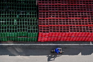 A man cycles past a huge stack of crates of bottled beer, half of them green and the other half red