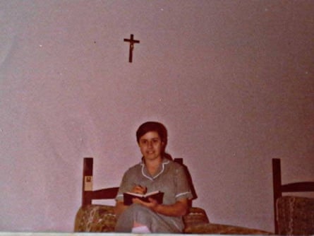 An old photo of a young woman in a maid’s uniform sitting on a bed reading in a dormitory with a crucifix on the wall
