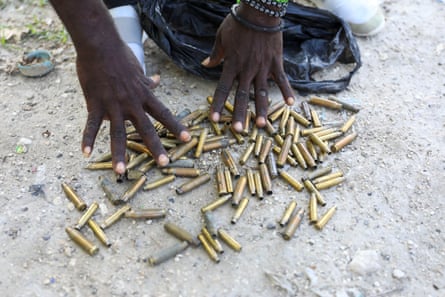 Two hands above dozens of long, brass bullet casings on the ground.