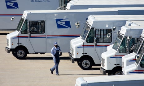 A mail carrier walks toward one of a line of boxy white US postal service trucks.