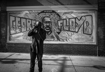 With a camera to his eye, the photographer stands in front of a wall bearing a memorial to George Floyd