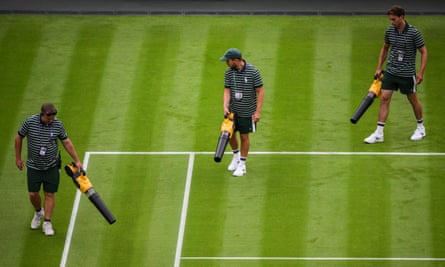 Wimbledon staff members use leaf blowers to dry the grass on Centre Court