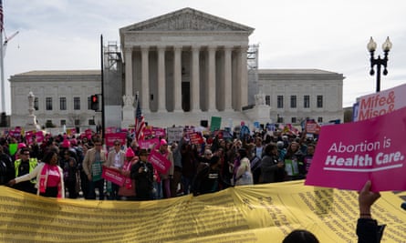A very long and wide yellow banner with black names on it amid crowds of people holding pink signs.