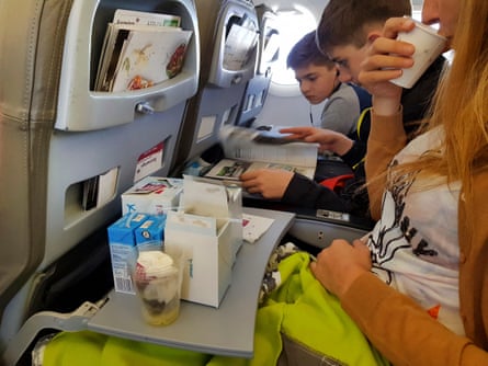 a woman and two children occupy three seats across an airplane row of seats