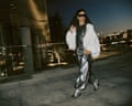 Woman walking in silver metallic pants and a wavy flowing white jacket with sunglasses at night on a concrete bridge or path