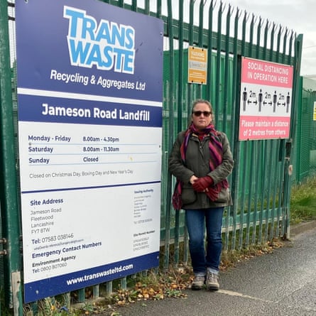 A woman stands beside a large gate with a sign saying ‘Transwaste’