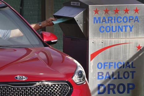 A car next to a ballot crop box with a hand dropping a ballot inside it.