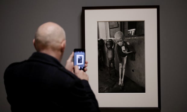 A visitor takes a photo of a 1968 photograph of a starving albino boy in Biafra by Don McCullin.