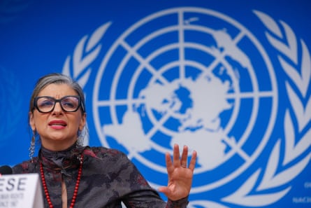 She sits at a table in front of a large UN map