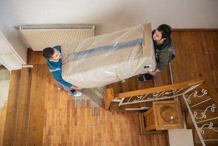 A shot from above shows two men carrying a piece of furniture up some stairs.