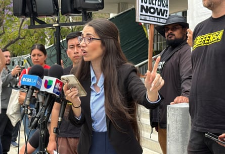 A woman speaks into microphones as she’s surrounded by supporters.