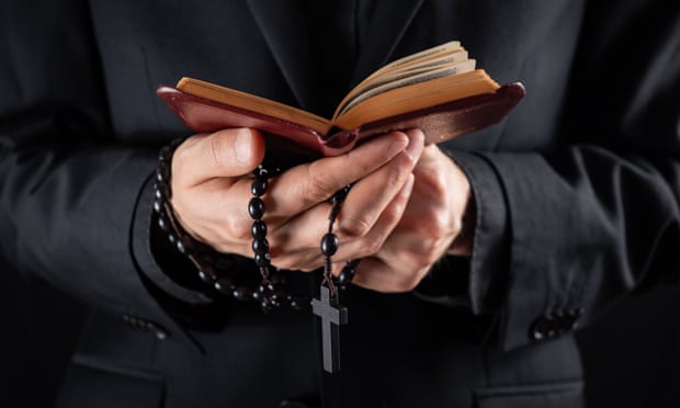 A priest's hands holding a crucifix and bible