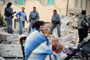 Victims sit among the rubble of a house
