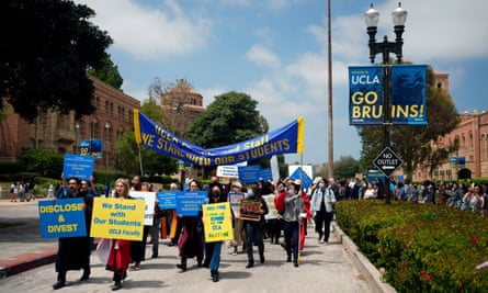 A parade of adults holding yellow and blue signs and a large overhead banner on a wide pathway.