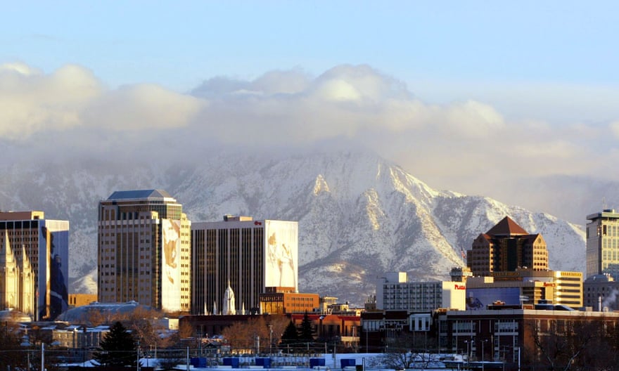 The downtown buildings of Salt Lake City glow in the setting sun with the Wasatch mountain range looming in the background.