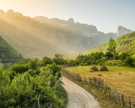 Early evening sun beams illuminate a valley with moutains and country lane