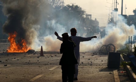 Two people stand silhouetted against a fire and a cloud of tear gas on a street in Peshawar