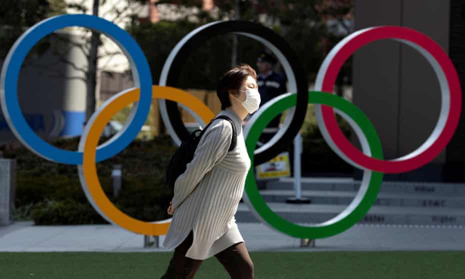 A woman wearing a protective face mask walks past the Olympic rings in Tokyo