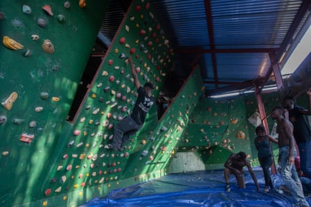 A man on an indoor climbing wall while four other men watch him