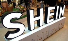 A large illuminated display reading 'Shein' with clothes rails in the background