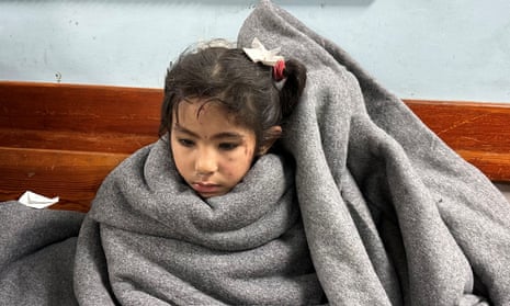 A girl wrapped in a grey blanket sits at a hospital in Rafah