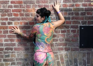 A tattooed visitor poses for photographs during the London Tattoo Convention at the Tobacco Dock, in London