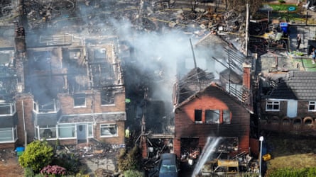 An aerial view of homes severely damaged by flames, with smoke still rising and roofs destroyed.