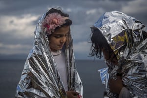 Two girls wear thermal blankets provided by volunteers after their arrival on the Greek island of Lesbos