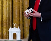 Trump holds white architectural arch models beside a similar model on a table