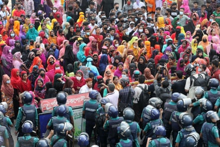 A crowd of mainly women wearing colourful head scarves faces a wall of riot police