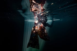 A diver near the surface of the water ties two mesh bags full of plastic bottles to a line