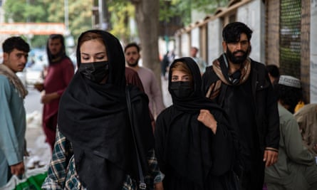 Women cover their faces while walking down a street in Kabul