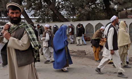 A burqa-clad Afghan woman walks among men in a market in Kabul