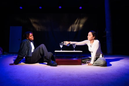Two women sit on the floor as one pours a drink