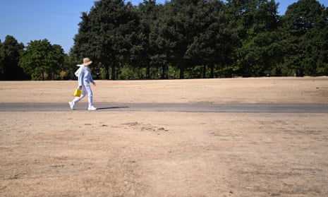 Woman in white walking over scorched grass in Hyde Park, London.