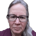 Unsmiling woman with glasses and long white hair