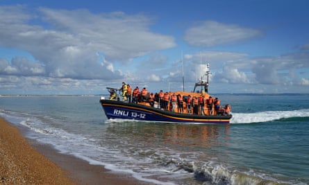 An RNLI lifeboat with many people standing on deck in lifejackets running up towards a shallow beach