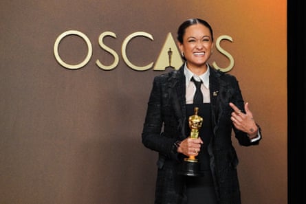 person wearing black suit gestures while holding gold statue award