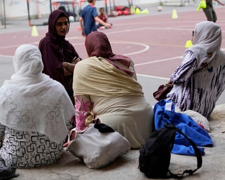 Women in headscarves chat as they sit next to a sports court